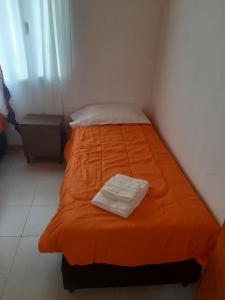 a small bed with an orange bedspread in a room at Alojamiento Río Fenix Chico in Perito Moreno