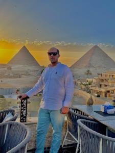 Un uomo è in piedi di fronte alle piramidi di pyramids guest house a Il Cairo