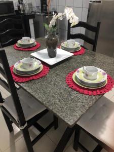 una mesa con platos y tazas y un jarrón con flores en Casa Completa Prox Centro de Pipa en Pipa