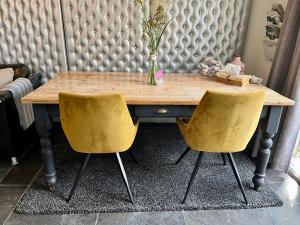 een houten tafel met twee gele stoelen voor een muur bij Bed & Breakfast "aan de banis" in Rijssen