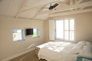 a white bedroom with a bed and a ceiling fan at The Lookout - Thesen Islands in Knysna
