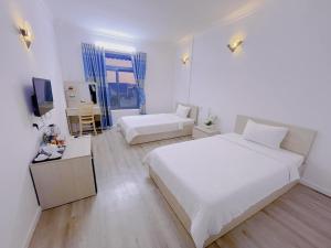a white bedroom with two beds and a television at Sai Gon Ha Tien Hotel in Hà Tiên