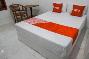 a bed with orange and white sheets and a chair at OYO 93161 Nurul Hikmah Homestay Syariah & Sport Center in Sedati