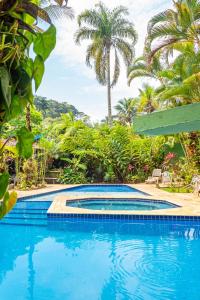 una piscina azul con palmeras en el fondo en Vila dos Tupinambás en Boicucanga