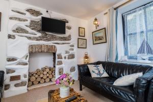 sala de estar con sofá de cuero negro y chimenea en Jessamine: Restored fisherman's cottage close to Looe's harbour, en Looe