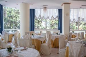 een eetkamer met witte tafels, stoelen en ramen bij Hotel Tridentum in Cesenatico