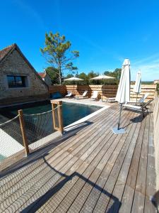 une terrasse en bois avec un parasol et une piscine dans l'établissement L'Escapade Authentique, à Brouchaud