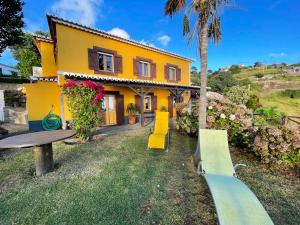 a yellow house with a table and a bench at 2 bedrooms house with sea view terrace and wifi at Faja da Ovelha 2 km away from the beach in Fajã da Ovelha