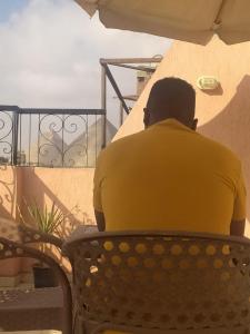 Un uomo con una camicia gialla seduto su una panchina di Pyramids Road Guest House a Il Cairo