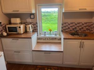 cocina con armarios blancos, fregadero y ventana en Daffodil Lodge en Sligo