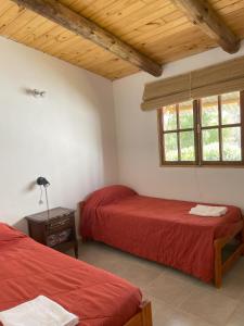 dwa łóżka w pokoju z czerwoną pościelą i oknem w obiekcie Cabañas Llitulun w mieście Alpa Corral