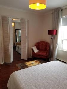 ein Schlafzimmer mit einem Bett und einem Stuhl sowie ein Wohnzimmer in der Unterkunft Logement avec stationnement tennis et piscine in Saguenay