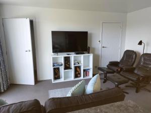uma sala de estar com um sofá e cadeiras e uma televisão de ecrã plano em Bethlehem Apartment em Tauranga