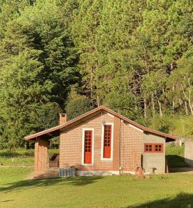 une petite maison en briques avec des portes rouges dans un champ dans l'établissement Chalé Vale das Minas Gerais, à Camanducaia
