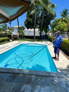 a man is mowing a pool with a hose at Linda Casa na Penha ! in Vera Cruz de Itaparica