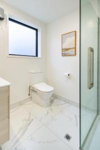 uma casa de banho branca com um WC e uma cabina de duche em vidro. em Gorgeous Getaway on Gloucester St- 1 Bed 1 Bath em Christchurch