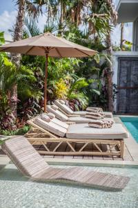 a group of lounge chairs and an umbrella next to a pool at Dreamy 5br Haven, 200m To Berawa's Blissful Beach in Canggu
