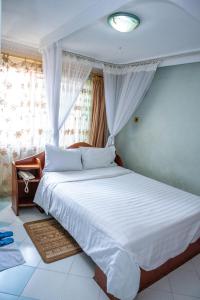 um quarto com uma cama com lençóis brancos e uma janela em Jupiter Guest Resort - Langata em Nairobi