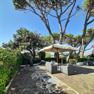 a patio with an umbrella and chairs and trees at Appartamento in Villa Valentini- Fronte mare, Giardino e Parcheggio privato, WIFI, dotato di tutti i confort, nel Cuore del Golfo di Gaeta in Minturno