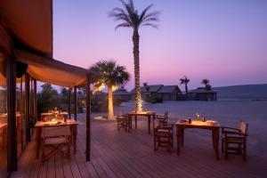 a deck with tables and chairs and a palm tree at The Outpost Al Barari in Mesaieed