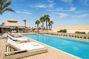 a resort pool with lounge chairs and a gazebo at The Outpost Al Barari in Mesaieed