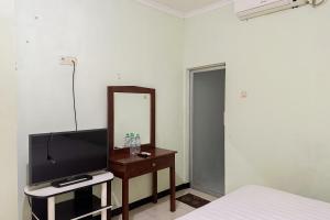 1 dormitorio con TV, espejo y cama en Global Inn Syariah Mitra RedDoorz near Juanda T1 Airport 
