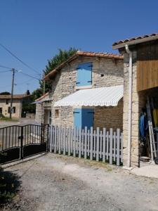 una casa de piedra con una valla blanca delante de ella en Gîte Bin Benaise linge compris, en Pamproux