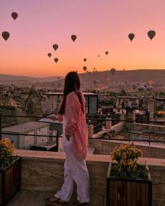 Una donna in piedi su un cornicione che guarda le mongolfiere di Emit Cave Hotel a Göreme