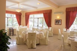 un restaurante con mesas y sillas blancas y ventanas en King's House Hotel Resort, en Mascali