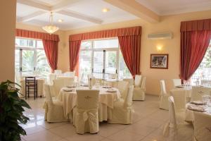 um restaurante com mesas e cadeiras brancas e janelas em King's House Hotel Resort em Mascali