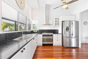cocina con armarios blancos y nevera de acero inoxidable en Private Resort-style Queenslander at Hervey Bay en Urangan