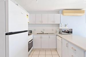a white kitchen with white cabinets and a refrigerator at Sandy Straits Poolside Escape with Beach Access in Hervey Bay