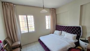 a bedroom with a bed with a purple headboard and two windows at Al Ahmer Apartments in Dubai