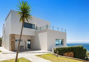 une maison blanche avec un palmier en face de l'océan dans l'établissement LUJOSAVILLA PISCINA 25 METROS SUIT 60m2 SPA SAUNA, à Zahara de los Atunes