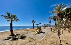 un parque infantil en una playa con palmeras y el océano en Apartamento de playa reformado, en Rincón de la Victoria