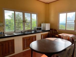 a kitchen with a table and a sink and two windows at Chaikho Home in Ban Khao Ya Nua