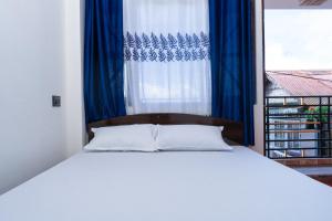Cama blanca con cortina azul y ventana en Bastola Basthan Homestay en Darjeeling