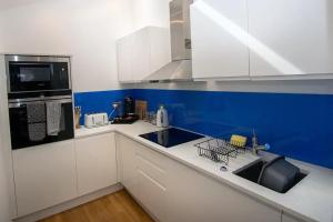 una cocina con armarios blancos y una pared azul en Seafront Cottage - The Nook en Cardiff