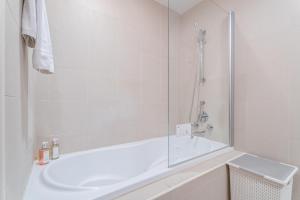La salle de bains blanche est pourvue d'une baignoire et d'une douche. dans l'établissement Nasma Luxury Stays - Sophisticated Studio Apartment near Burj Khalifa, à Dubaï