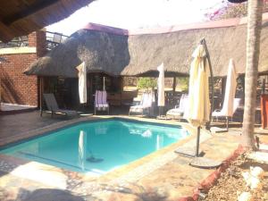 a swimming pool with an umbrella and chairs and a table at One & Only Bush Lodge in Bela-Bela