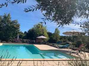 a swimming pool with an umbrella and chairs at Coutillard in Parisot-Tarn-et-Garonne