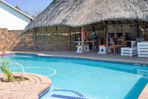 a large swimming pool with a thatch roof at Woodpecker's Inn Guest House in Kempton Park