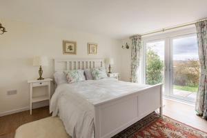 Dormitorio blanco con cama y ventana grande en Oak Tree Cottage, en Uckfield