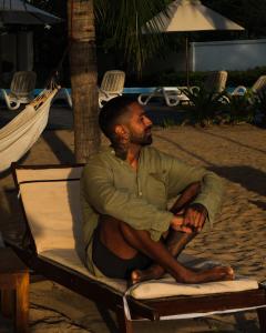 a man sitting in a chair on the beach at Cardamon Hotel Nilaveli in Nilaveli