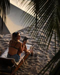 Cardamon Hotel Nilaveli في نيلافيلي: امرأة تجلس على كرسي الشاطئ تقرأ الكتاب