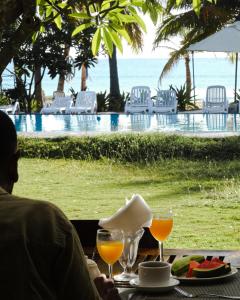 un hombre sentado en una mesa con vasos de jugo de naranja en Cardamon Hotel Nilaveli en Nilaveli