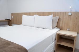 1 cama con sábanas blancas y almohadas en una habitación en Pousada Areia do Forte, en Cabo Frío