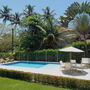 uma piscina com cadeiras e um guarda-sol e palmeiras em Villa Rossella em Morro de São Paulo