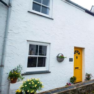 a white building with a yellow door and a window at Sea Shanty Cottage in Newlyn