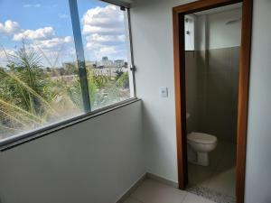 a bathroom with a toilet and a large window at Comfort 302 - 4 Quartos no Centro in Sete Lagoas